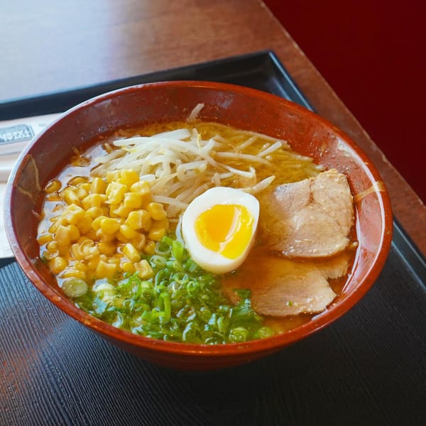 A bowl of Ramen Ray ramen with corn, bean sprouts, pork, green onions, and a soft-boiled egg.