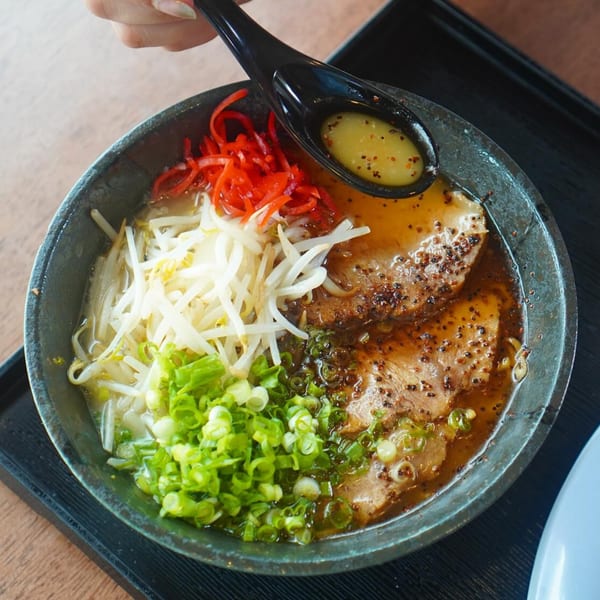 A bowl of Ramen Ray's ramen with pork, bean sprouts, green onions, and red ginger.